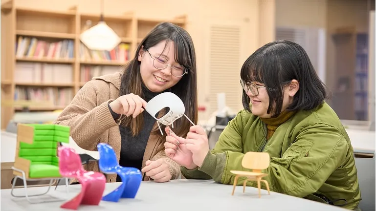 小さな椅子を手に取りながら会話をする学生たち