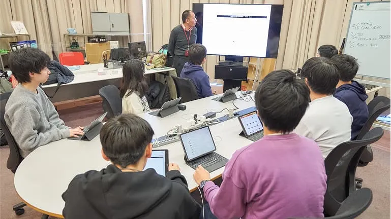 モニターを見て先生の話を聞く学生たち