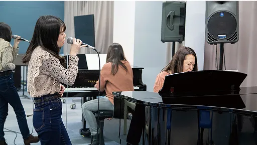 学生が講師のピアノに合わせてマイクで発声する様子