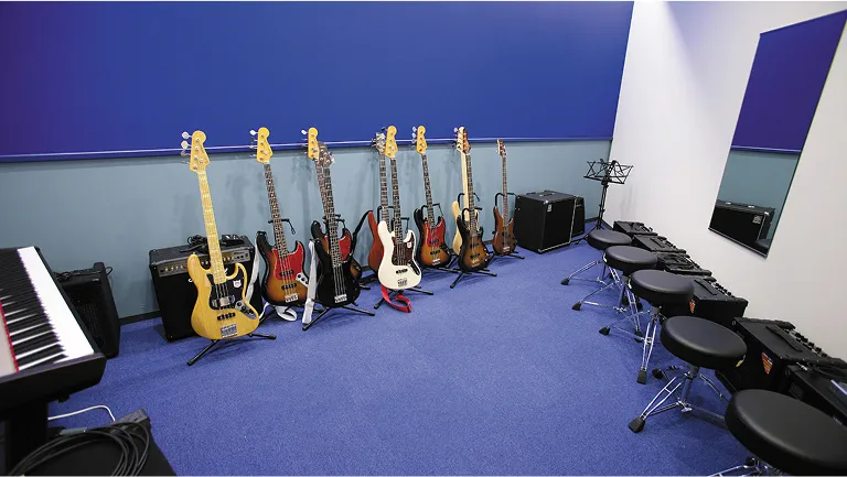 複数の楽器、アンプが設置された青い壁と青いカーペットが特徴的な実習室