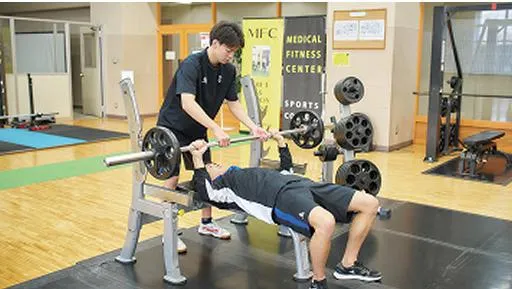 ベンチプレスを上げる生徒と補助をするコーチ