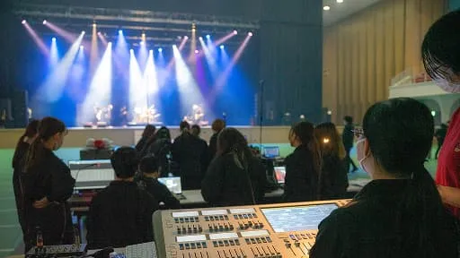 学生たちがステージを見ながら音響や照明などの機材を操作する様子