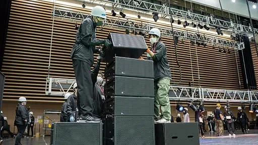 学生たちがヘルメットを着用し音響機器の設置作業を行っている様子