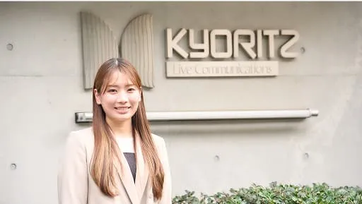 社名看板の前で話す小谷津 美花さん