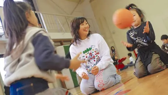 座って子供とボール遊びをしている笑顔の生徒