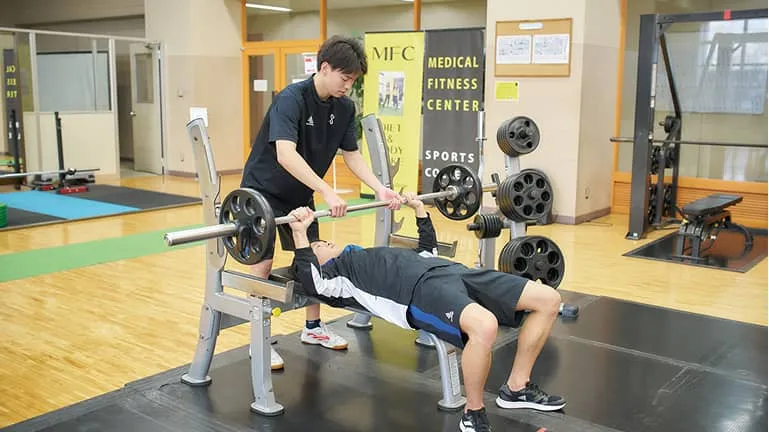 ベンチプレスをする生徒と補助をするコーチ