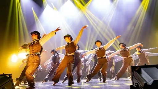 スポットライトの下で腕を広げ、ポーズを決めるジャズダンスチーム