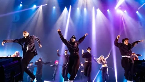 照明が当たったステージで躍動的なダンスを披露するダンスチーム