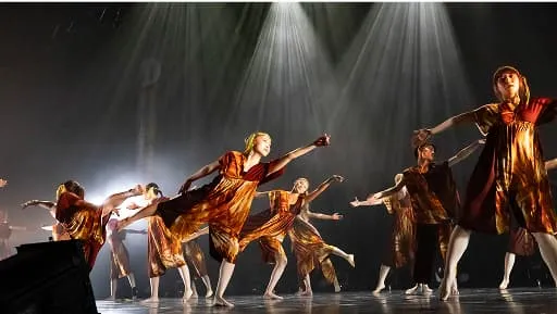 スポットライトの下で腕を広げ、ポーズを決めるコンテンポラリーダンスチーム