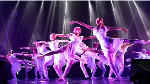 スポットライトの下で腕を広げ、ポーズを決めるクラシックバレエチーム