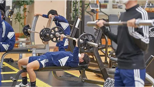 ベンチプレスでトレーニングをする生徒と各々トレーニングをする生徒たち