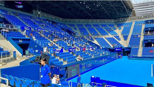 テニスの試合が行われている会場で、観戦している観客と観客席の前に立つスタッフの様子