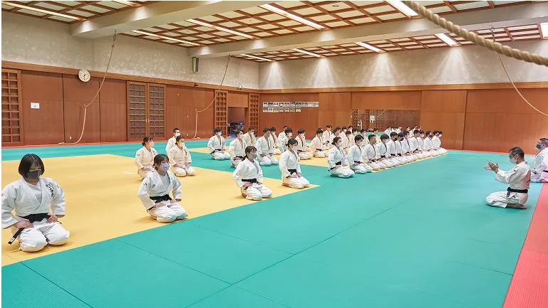 大勢の学生たちが講師と共に武道場で正座をしている様子