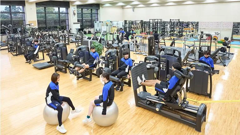 沢山のトレーニングマシンが設置されている広い室内で学生たちがトレーニングをしている様子