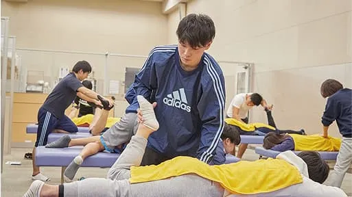 学生たちがベッドに横になっている人に整体をしている様子