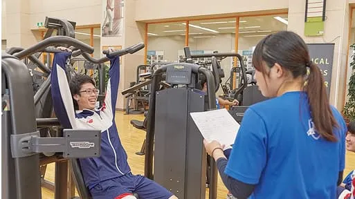 学生がトレーニングマシンを使用している人のサポートをしている様子