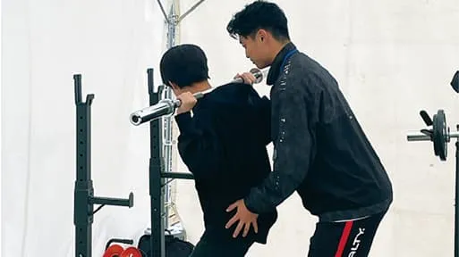 トレーニングマシンを使用している人と、後ろからサポートをしている人の様子