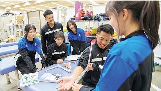 女性が男性の腕を測定しているところを学生たちが見ている様子