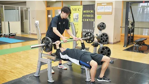 トレーニングマシンを使用している男性とサポートをしている男性の様子