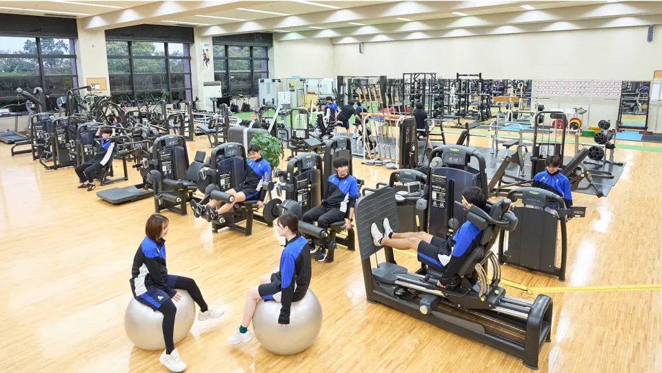 沢山のトレーニングマシンが設置されている広い室内で学生たちがトレーニングをしている様子