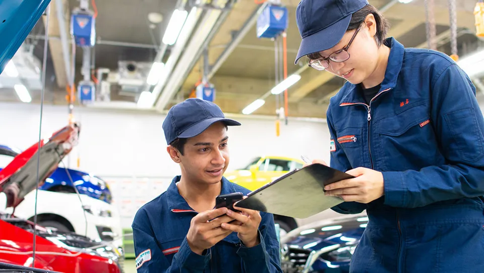 自動車の前でメモを取っている学生と、端末を手に持ちその様子を見ている学生