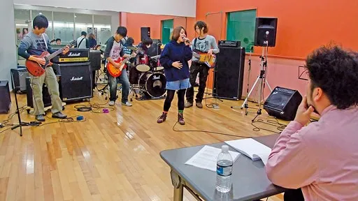スタジオで企業担当者が学生バンドの演奏を聴く様子