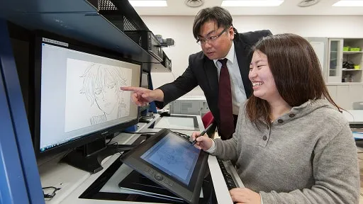 パソコンで制作を行う学生に講師が指導する様子