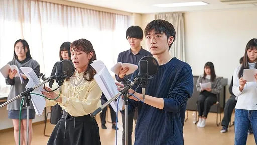 学生たちがマイクに向かい台本持って演じている様子