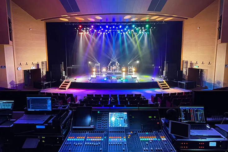 音響機器が並ぶPA席から、カラフルな照明が光るステージを臨む風景