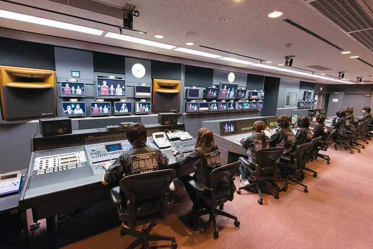 使用しているすべてのカメラ映像が映る複数のモニターと、音響ミキサーやタイムキーパーなど役割ごとの席に生徒達ついているいる風景