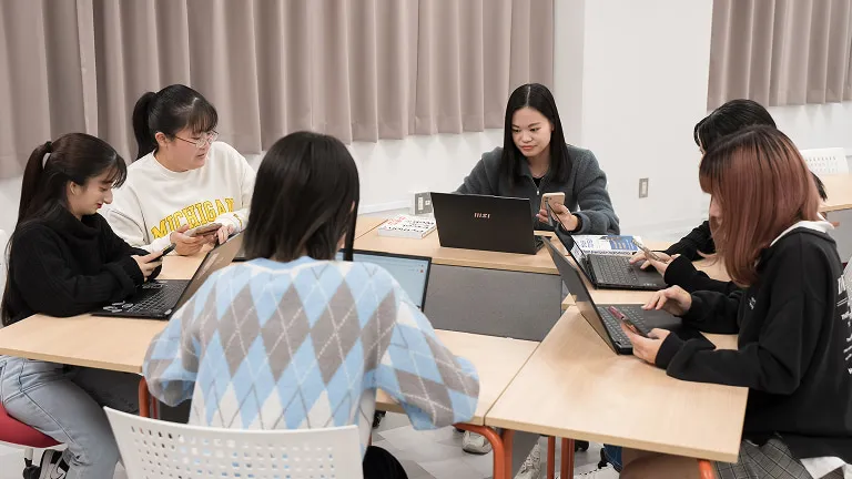 学生グループがスマートフォンやパソコンを使用する様子
