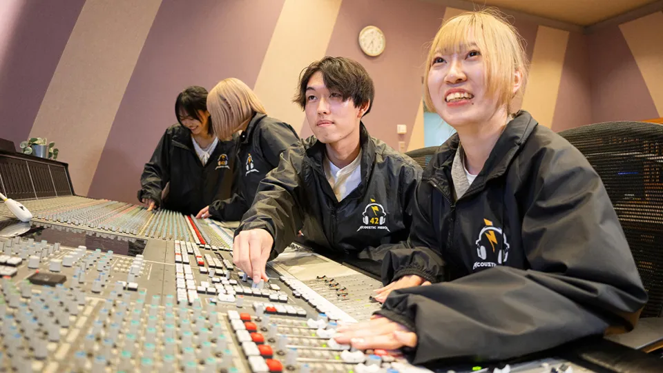 学生が録音スタジオでミキシング卓を使いながら音響技術を学んでいる様子