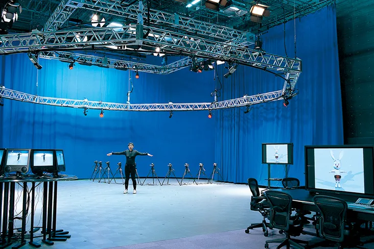 青い幕が壁沿いに張られ、カメラに頭上から360度を囲まれた演技者の動きが、PCデスク側のCGキャラクターに反映されている風景