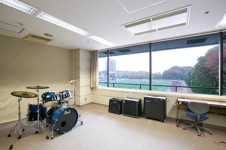 ドラムセットやアンプが設置された、窓の外に総合グラウンドを臨む室内