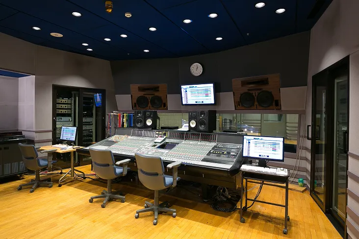 大きなミキサーテーブルを中心に高度な音響機器が並び、奥に収録用の部屋が見える様子