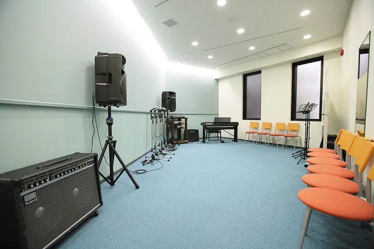 淡い青が中心の涼しげな広い室内にキーボードやスタンド型のスピーカーが配置されている悠々とした環境