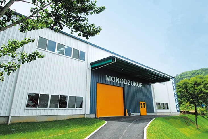 白、紺、オレンジの配色にローマ字でものづくり工房と掲示された工場にも見える大型施設