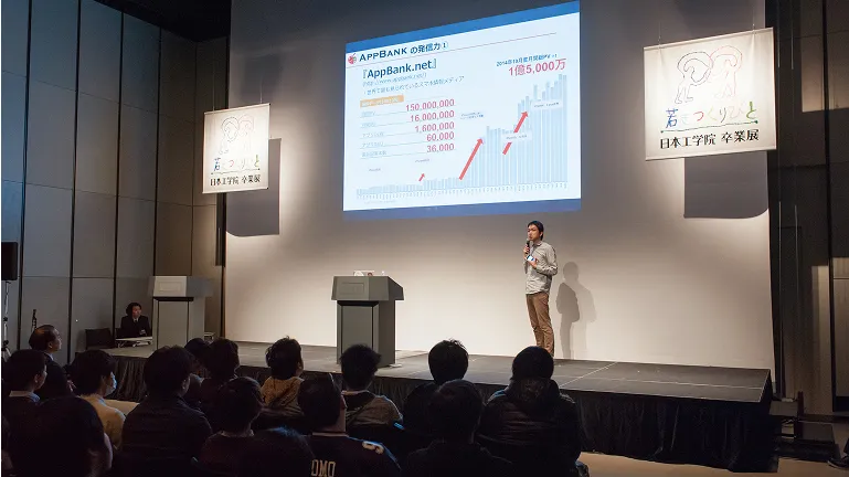 スクリーンを使ったプレゼンテーションがステージで行われる様子