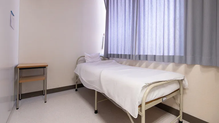 ベッドと小さなデスクが設置し明るさを抑えた個室