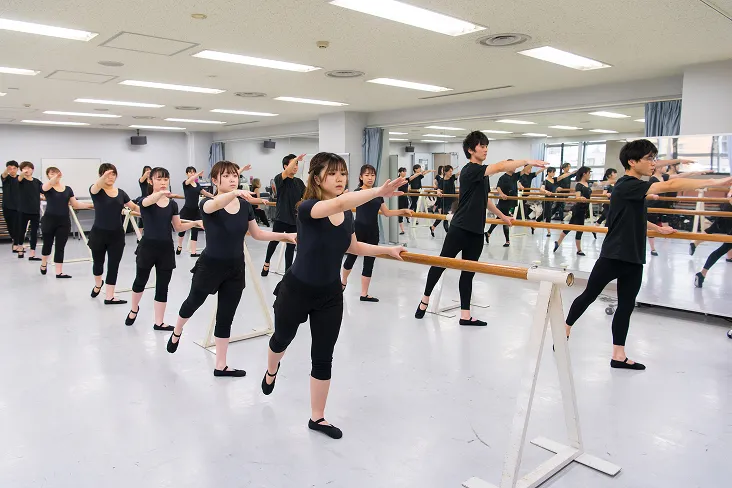 片手でバレエバーを掴みバレエのレッスンを受ける生徒達の様子