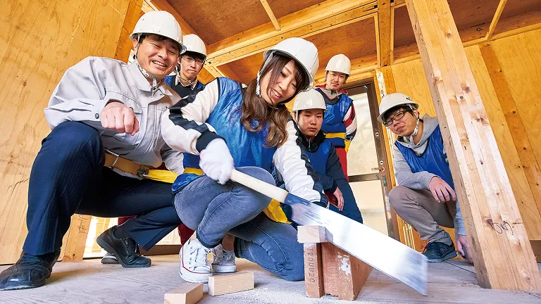 女性が木材をカットしているところを後ろから学生たちが見ている様子