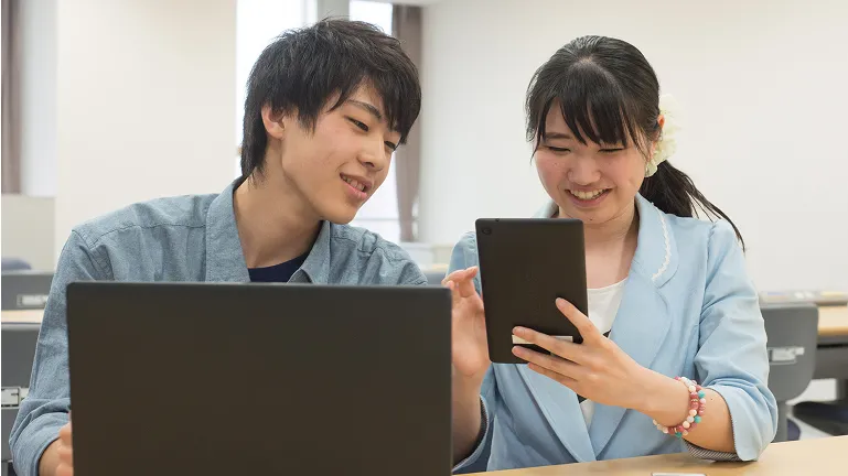 学生がタブレットとパソコンを見ながら会話する様子