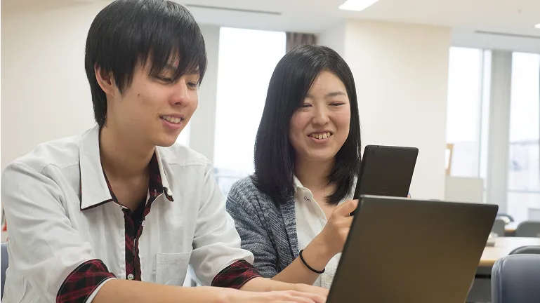 学生がスマートフォンとパソコンを見ながら会話する様子
