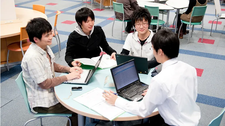 学生たちが丸いテーブルにノートパソコンを持ち寄って学習する様子