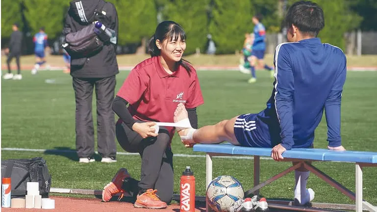 学生がベンチに座っている人の足にテーピングをしている様子