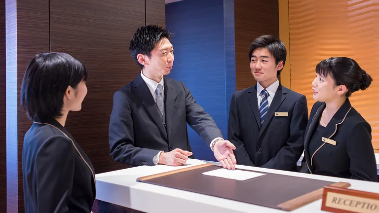 学生たちが実習で講師からフロントでの接客について学ぶ様子