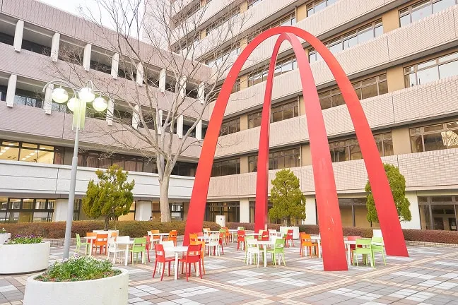 交差する赤い半円のオブジェを見上げる形の屋外席が並んだ風景