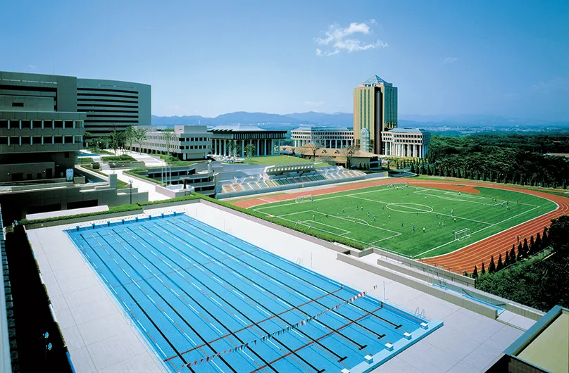 階段状の観客席を持つ総合グラウンドと8レーンあるプールの風景