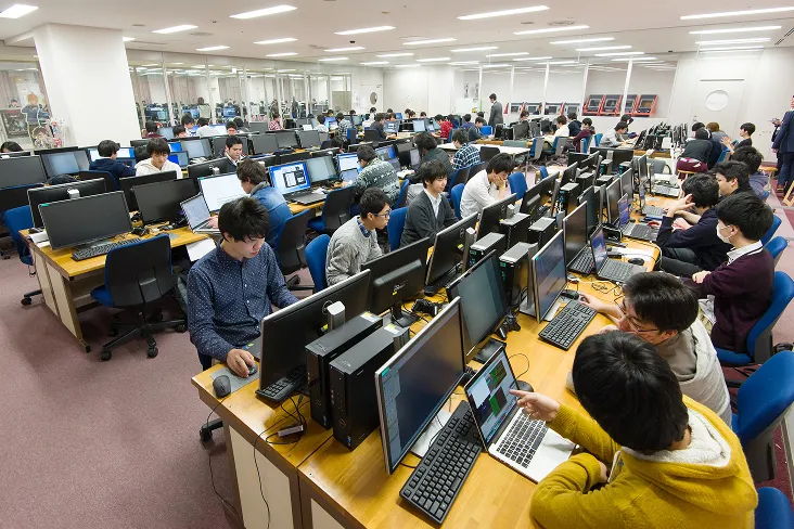 2席に対して3枚のディスプレイが設置され、更にノートPCを開いても余裕がある大型テーブルが並んだゲーム制作スタジオの授業風景