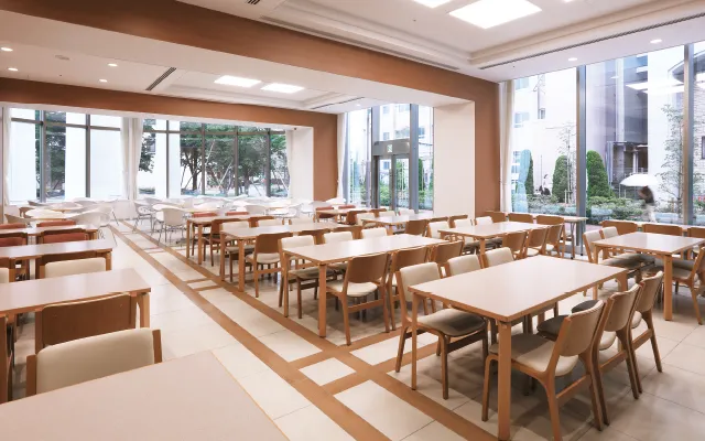 木製のしっかりしたテーブルセットが並ぶ、ベージュと明るい茶色でまとめられた温かみのある室内